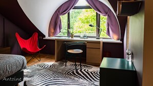A bedroom with a curved ceiling, a desk, a red chair, a zebra-patterned rug, and a window with purple curtains. - La Petite Bruyere De Renaix (Ronse)