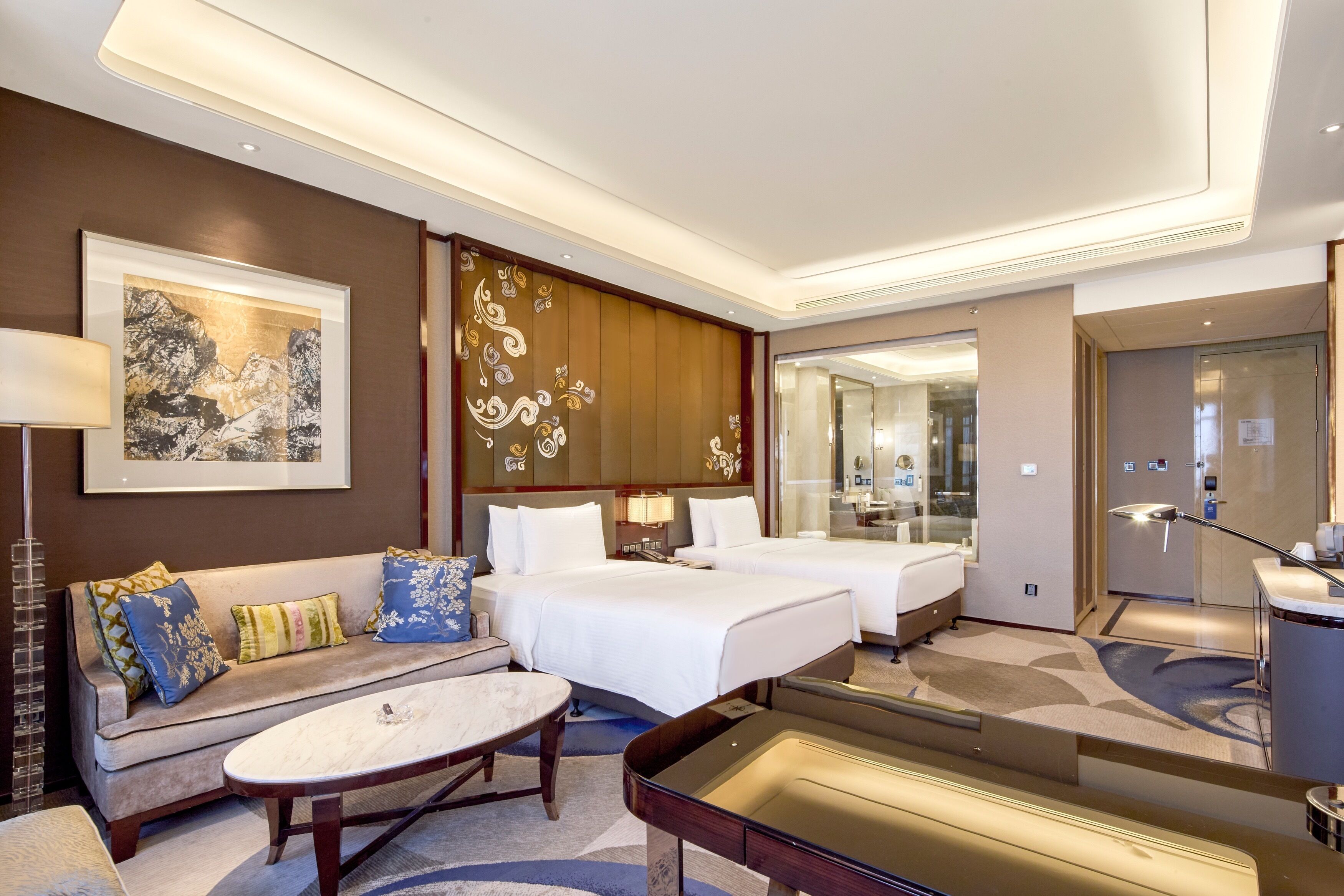 A hotel room with two beds, a sofa, a coffee table, and a decorative wall panel.