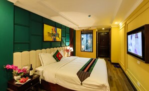 A hotel room with a bed, a television, a nightstand with a bottle of wine and glasses, and a painting on the wall. - Sapa Clover Hotel (Sa Pa)