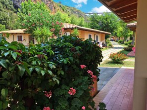 A courtyard with a covered seating area, a pathway leading to a building with a tiled roof, and lush greenery. - Arcomagno Hotel Village Club (San Nicola Arcella)
