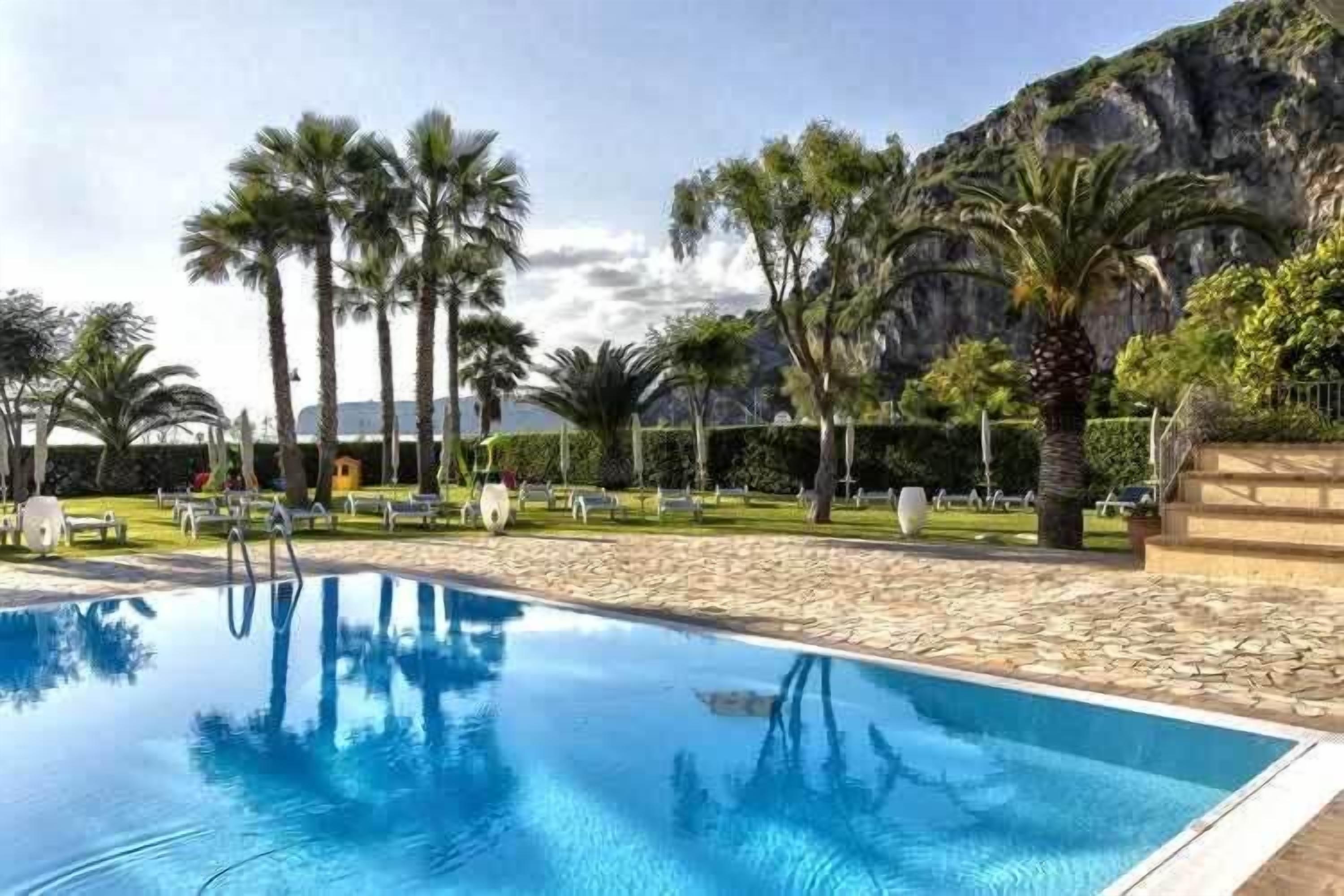 Una piscina con acqua cristallina blu, circondata da palme e con montagne sullo sfondo.