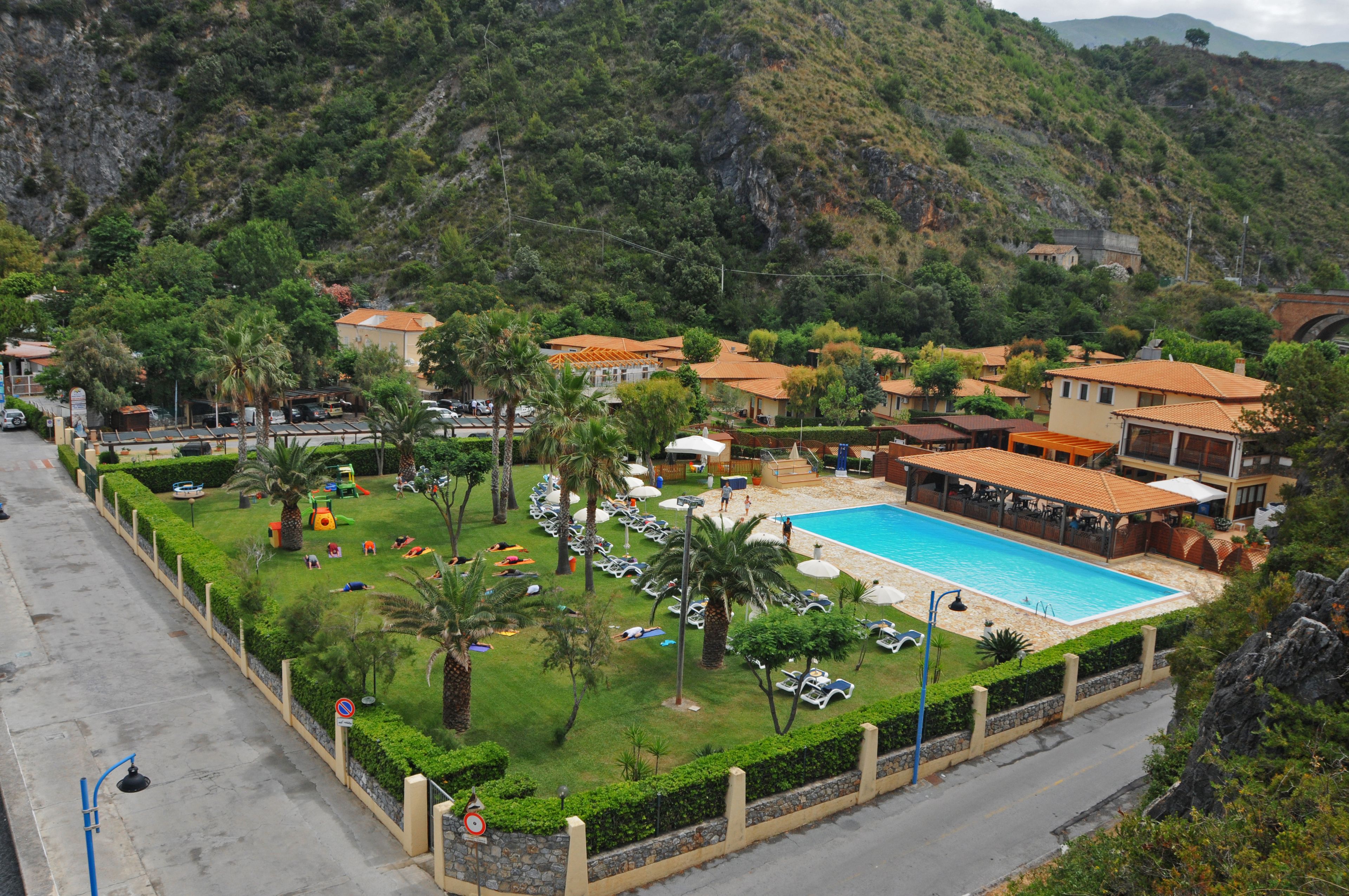 Un resort con piscina, vegetazione lussureggiante e montagne sullo sfondo.