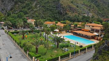 Un resort con piscina, vegetazione lussureggiante e montagne sullo sfondo.