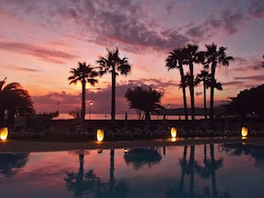 A poolside view at dusk with palm trees and lounge chairs. - Arcomagno Hotel Village Club (San Nicola Arcella)