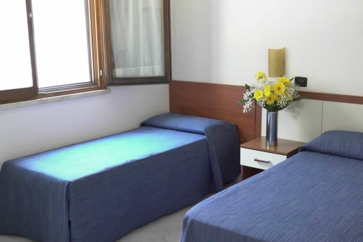 Una habitación de hotel con dos camas individuales, una mesita de noche con lámpara y un jarrón con flores.