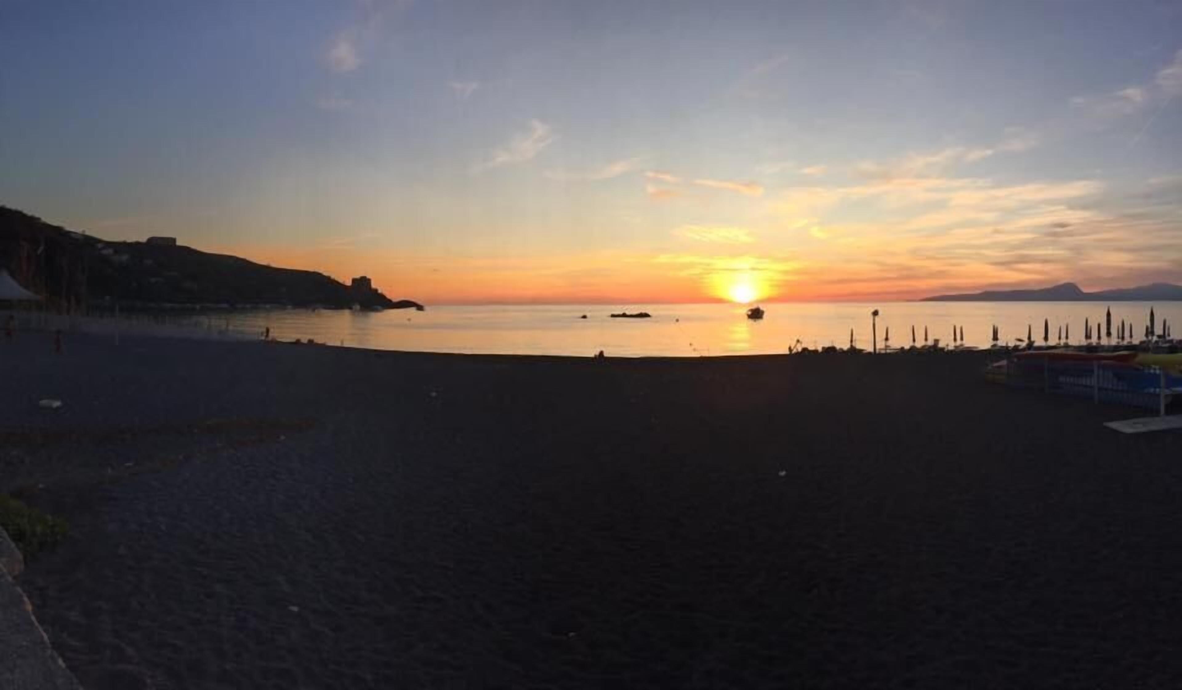 Una spiaggia al tramonto con mare calmo, montagne in lontananza e una fila di ombrelloni.