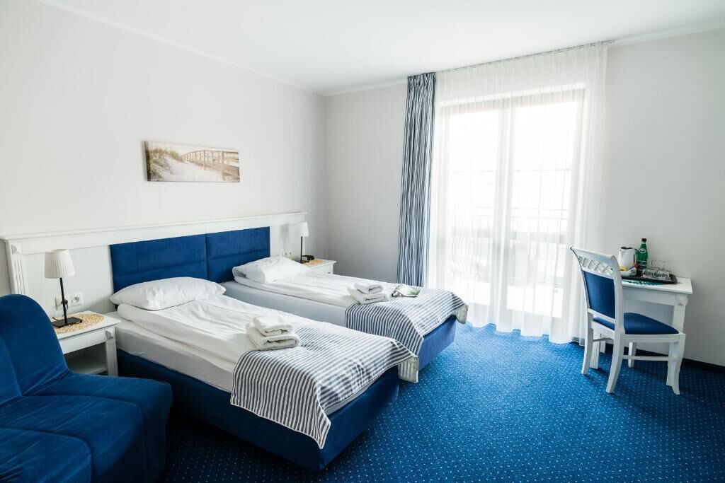 A hotel room with two beds, a desk, a chair, and a window with curtains.