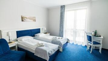 A hotel room with two beds, a desk, a chair, and a window with curtains.