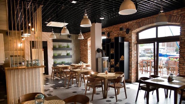 Ein Restaurant mit sechseckigem Bodenmuster, Holztischen und -stühlen, hängenden Pendelleuchten und Backsteinwänden.