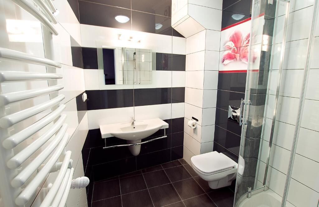 A modern bathroom with a white sink, black and white tiles, a glass shower enclosure, and a white toilet.