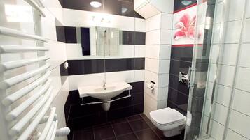 A modern bathroom with a white sink, black and white tiles, a glass shower enclosure, and a white toilet.