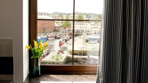 Blick aus dem Fenster auf einen belebten Hafen mit Booten, einem Kran und Gebäuden im Hintergrund.