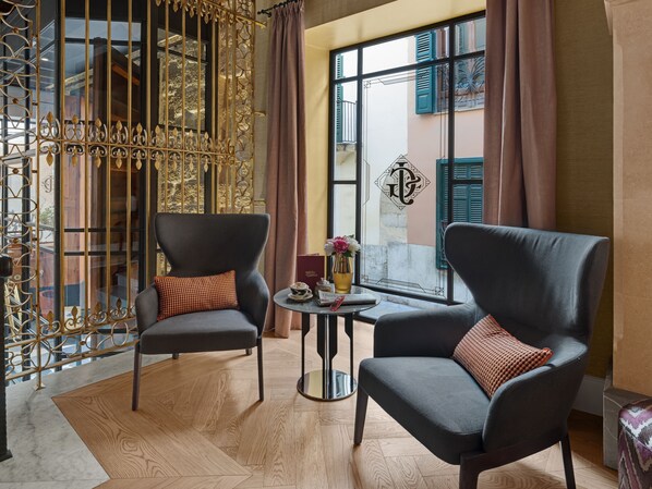 A room with two armchairs, a small round table with a vase and a book, and a window with shutters. - Hotel Glòria de Sant Jaume (Palma de Mallorca)