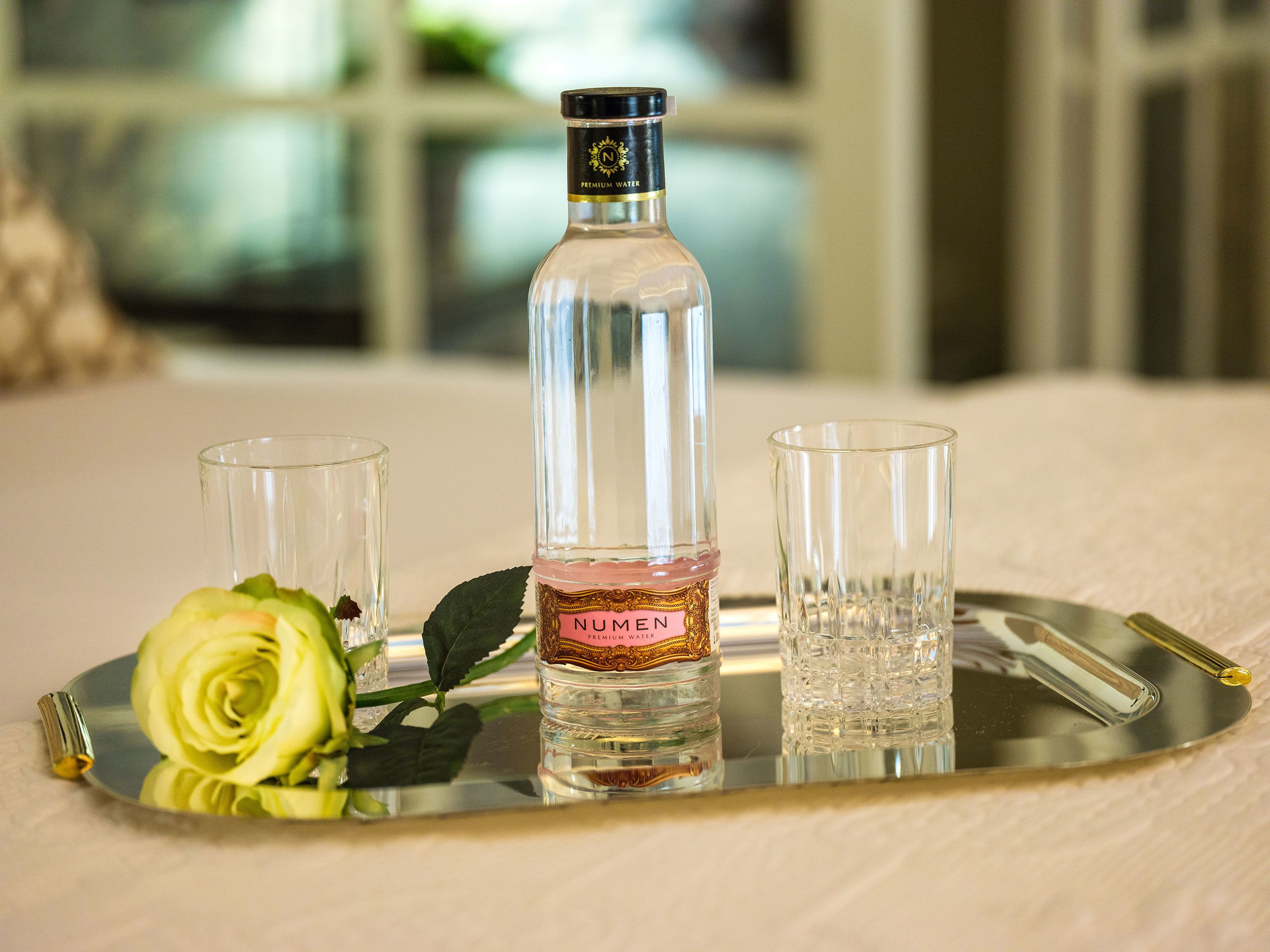 Une bouteille d’eau minérale Numener, présentée sur un plateau avec deux verres et une rose.