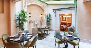 A dining area with tables set for four, surrounded by chairs, and a view of a restaurant through an open archway. - Hotel Glòria de Sant Jaume (Palma de Mallorca)