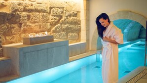 A spa area with a stone wall, a heated pool, and a person in a bathrobe standing by the pool. - Hotel Glòria de Sant Jaume (Palma de Mallorca)