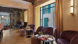 A modern lounge area with plush seating, a coffee table with breakfast items, and a view of the city through large windows. - Hotel Glòria de Sant Jaume (Palma de Mallorca)
