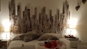 A neatly made bed with pillows and a blanket, a bedside table with a lamp, and a wall with a rustic wooden panel design. - Il Mare di Roma (Rome)