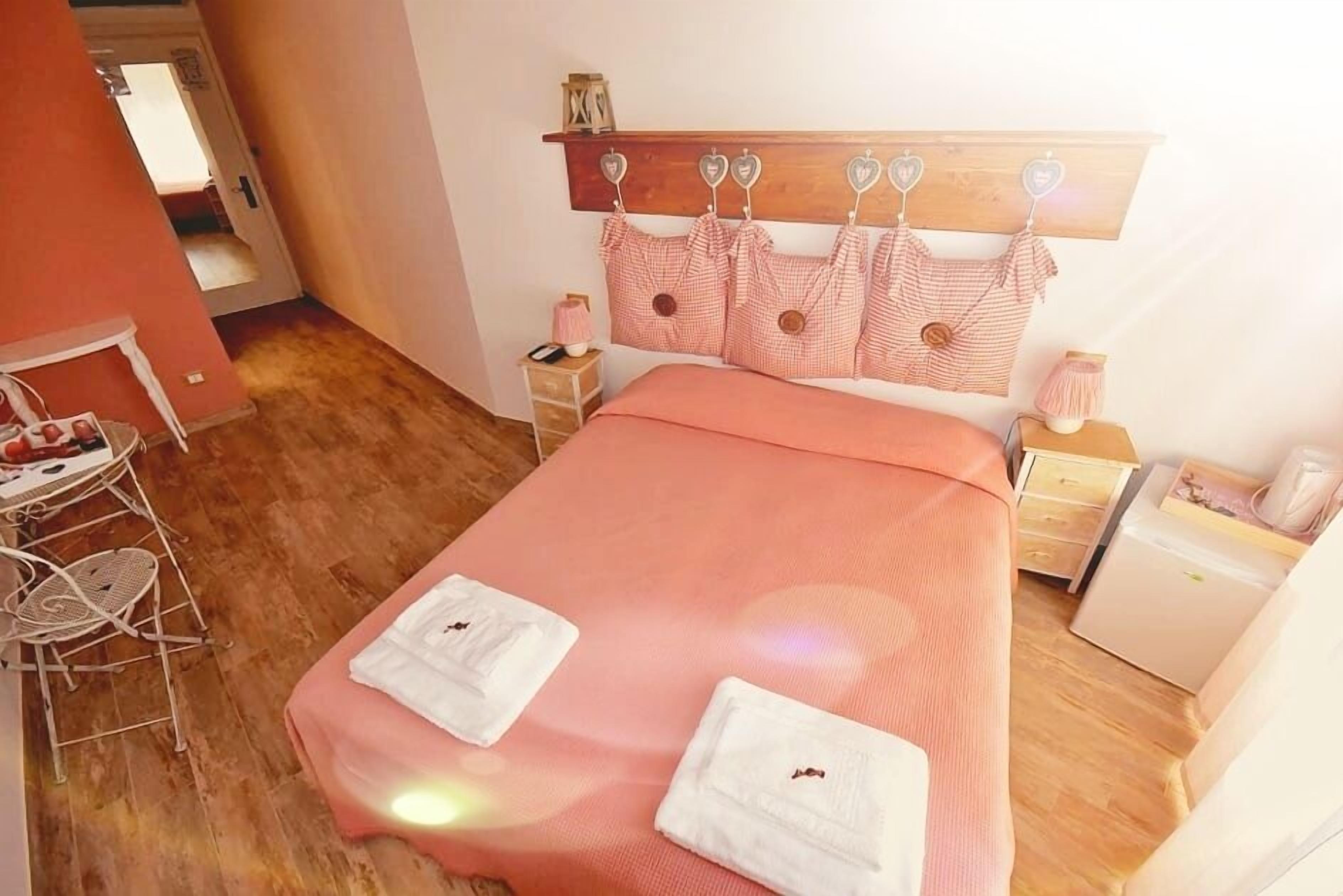 Une chambre à coucher bien rangée, avec une tête de lit en bois, une couvre-lit rose et deux serviettes blanches sur le lit.