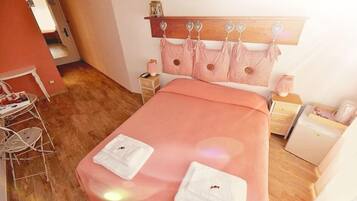 Une chambre à coucher bien rangée, avec une tête de lit en bois, une couvre-lit rose et deux serviettes blanches sur le lit.