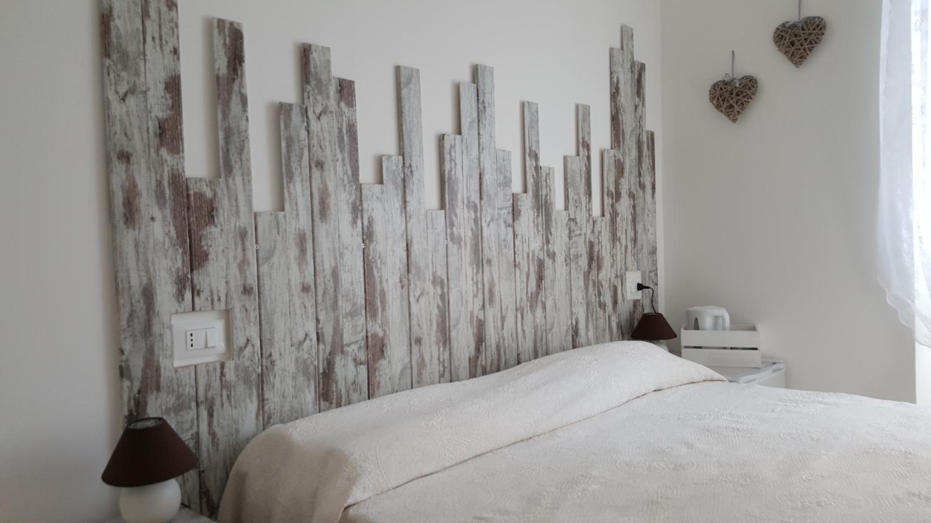 A bedroom with a rustic wooden headboard, a bed with a white bedspread, two bedside lamps, and a small bedside table with a lamp.