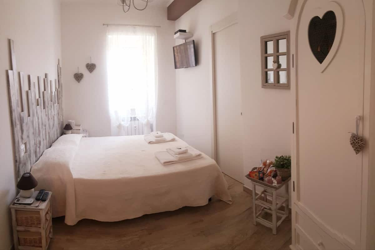 Ein Schlafzimmer mit einem großen Bett, einem Fernseher, einer herzförmigen Dekoration und einem kleinen Tisch mit Gegenständen darauf.