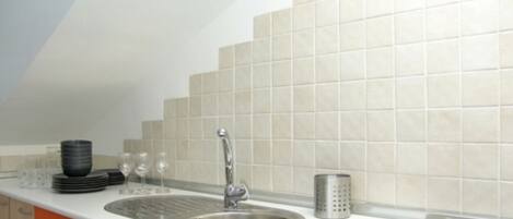 Una cocina con un lavamanos de acero inoxidable, estufa integrada y salpicadero de azulejos.