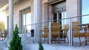 Hotel amb una zona d'estar exterior coberta, una escala que condueix a l'entrada i un jardí ben cuidat amb diverses plantes i una roca decorativa.