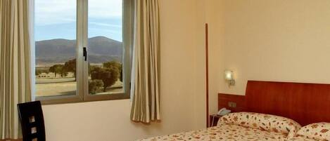 Habitación de hotel con cama, una silla, una mesita de noche y una ventana con cortinas.