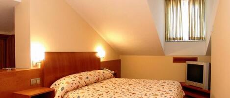 A bedroom with a bed, a bedside table, a TV, and a window with curtains.