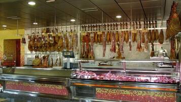 Zona de exhibición de embutidos con varios tipos de carne curada colgada en ganchos y un mostrador con salpicadero de azulejos.