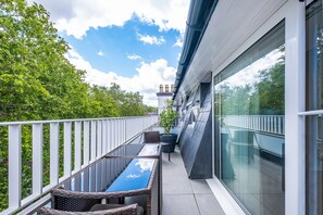 A balcony with wicker furniture, a potted plant, and a view of trees and a building. - Lak Serviced Apartments (London)