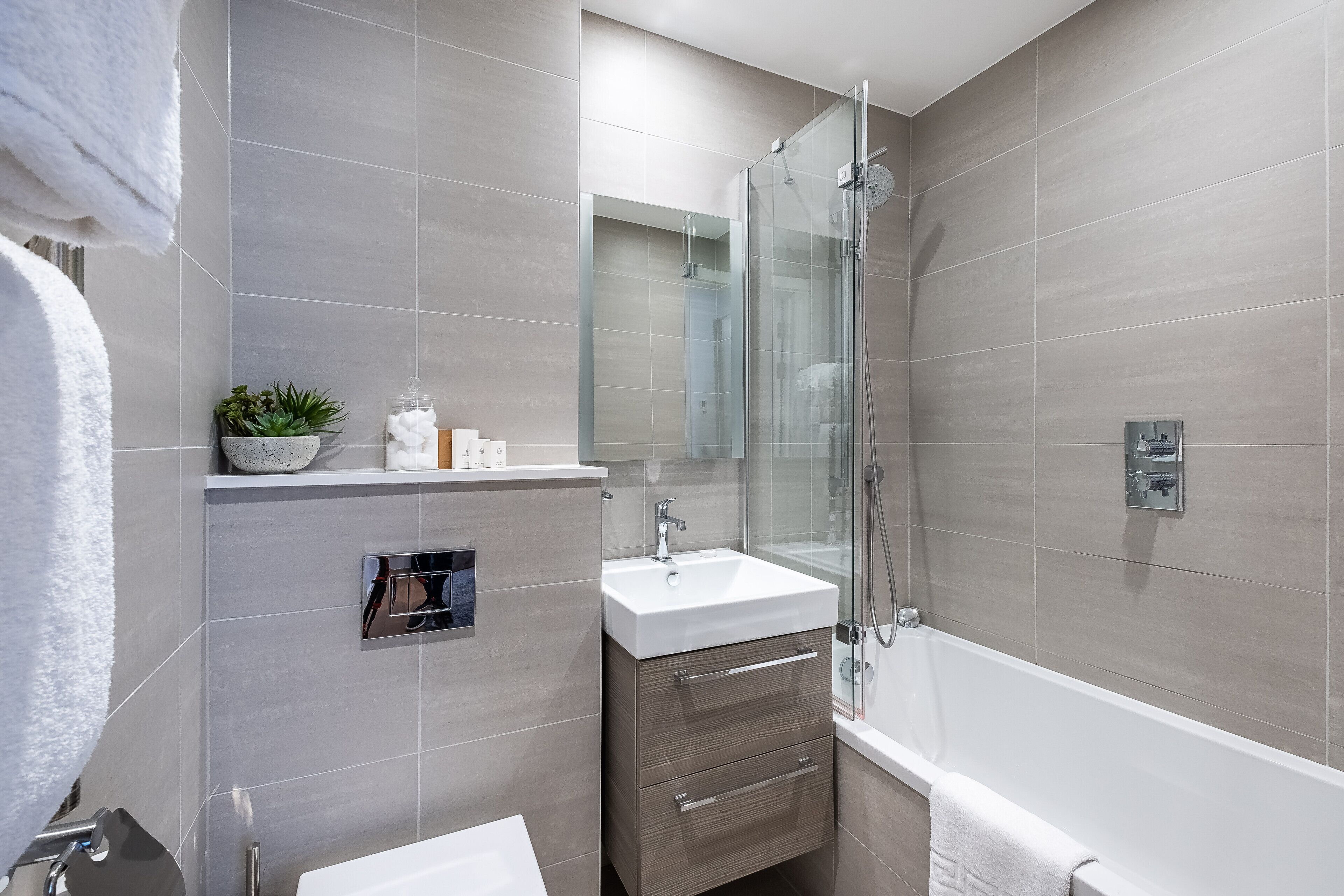 A modern bathroom with a glass-enclosed shower, a white sink, and a built-in vanity with drawers.
