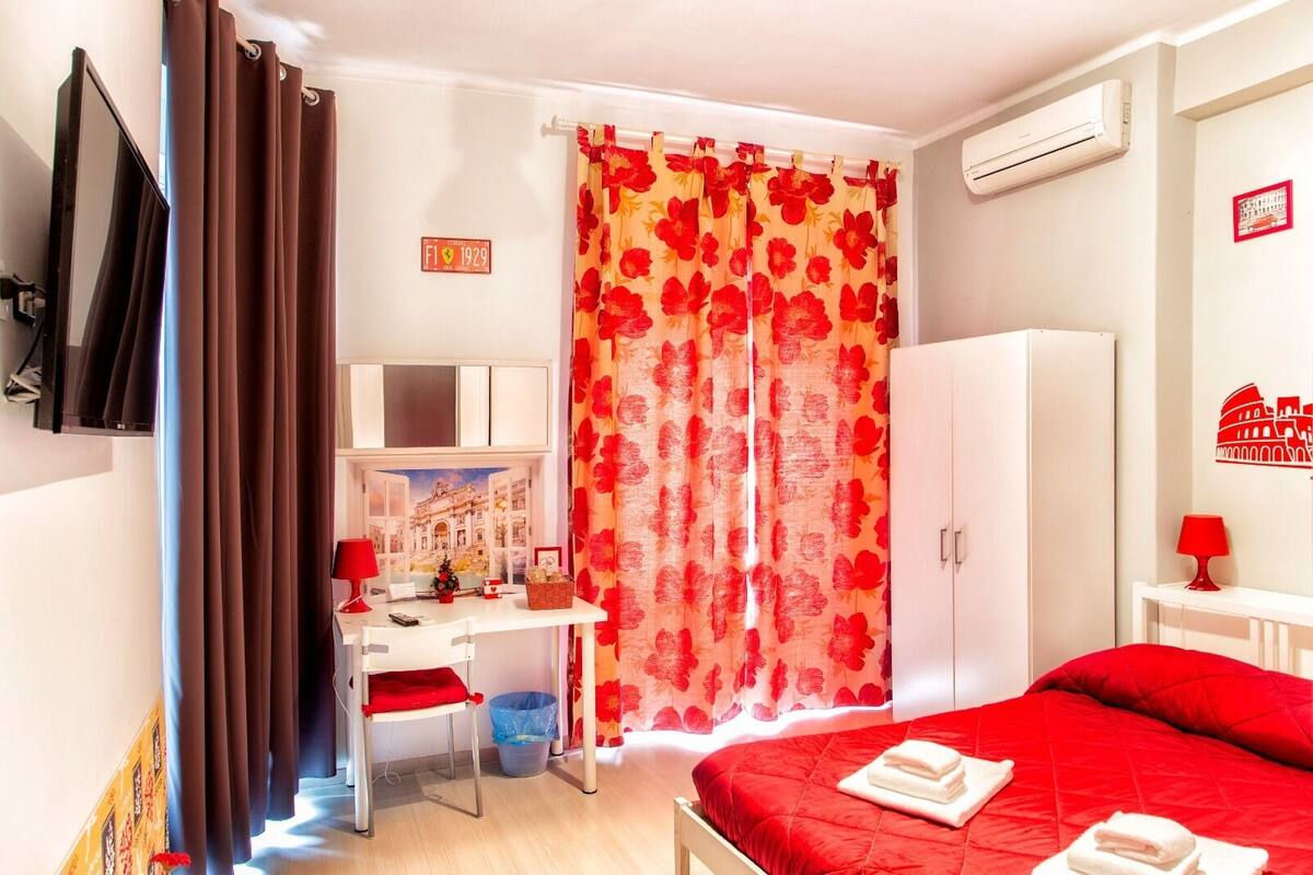 A hotel room with a bed, a desk with a chair, a wardrobe, and a shower curtain with a floral pattern.
