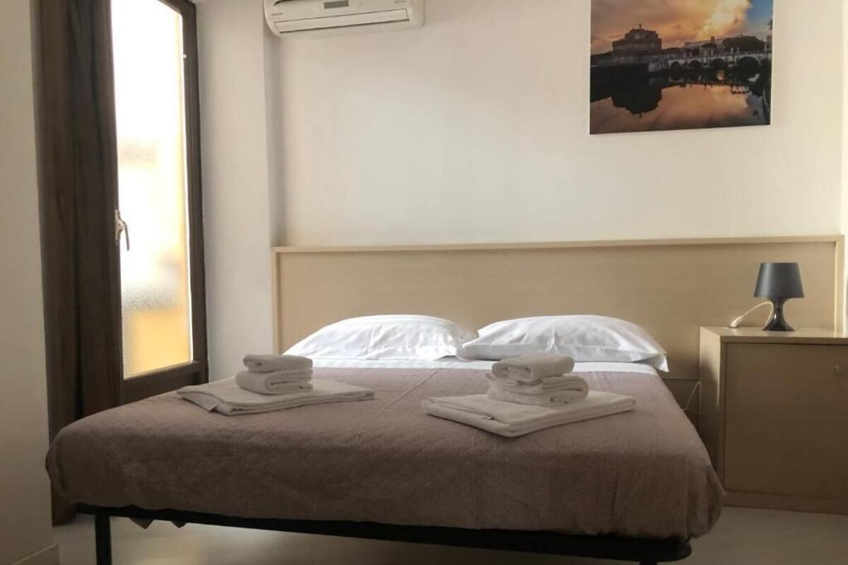 A hotel room with a bed, two pillows, a nightstand with a lamp, and a painting on the wall.