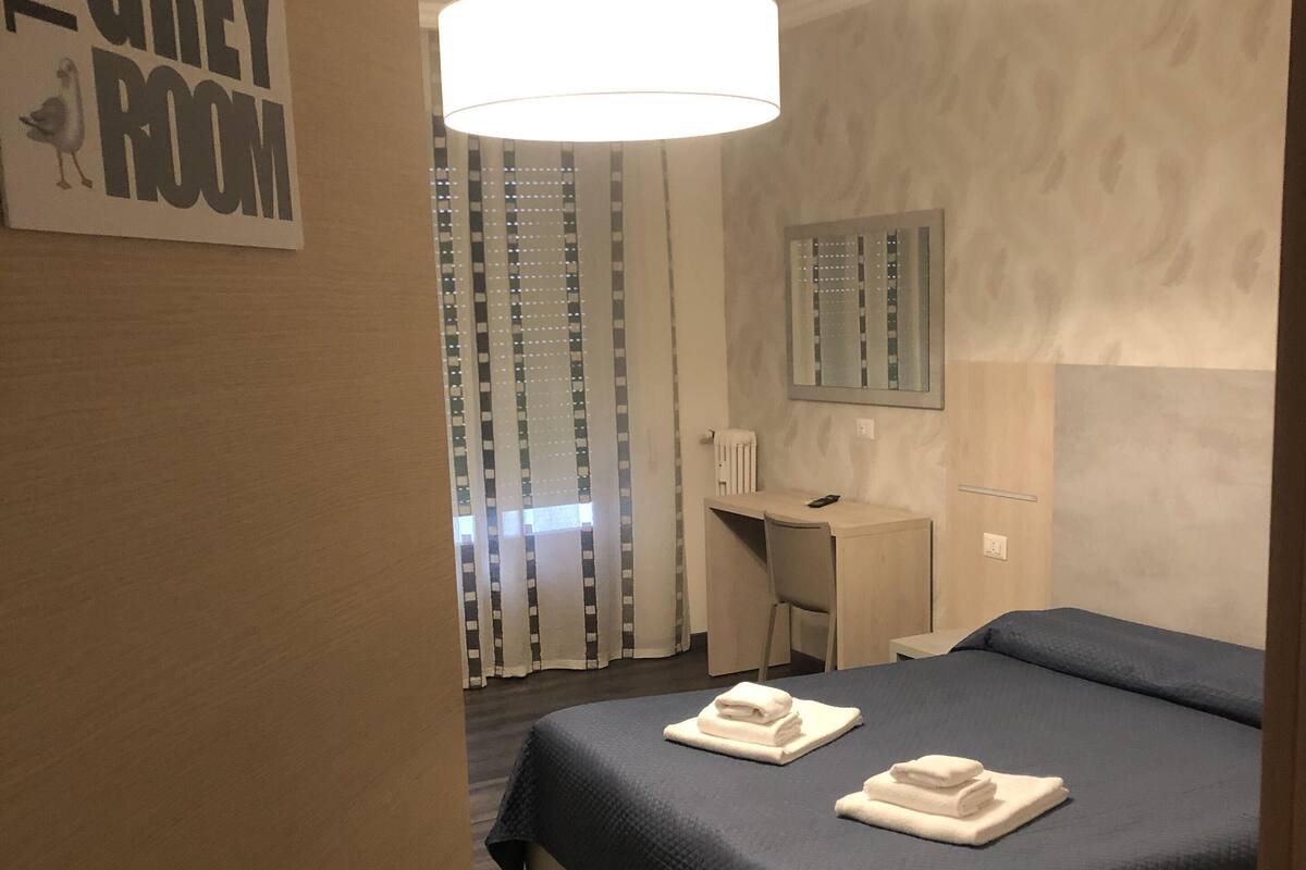 A hotel room with a bed, a desk, and a chair. There is a sign on the wall that reads "GREY ROOM".