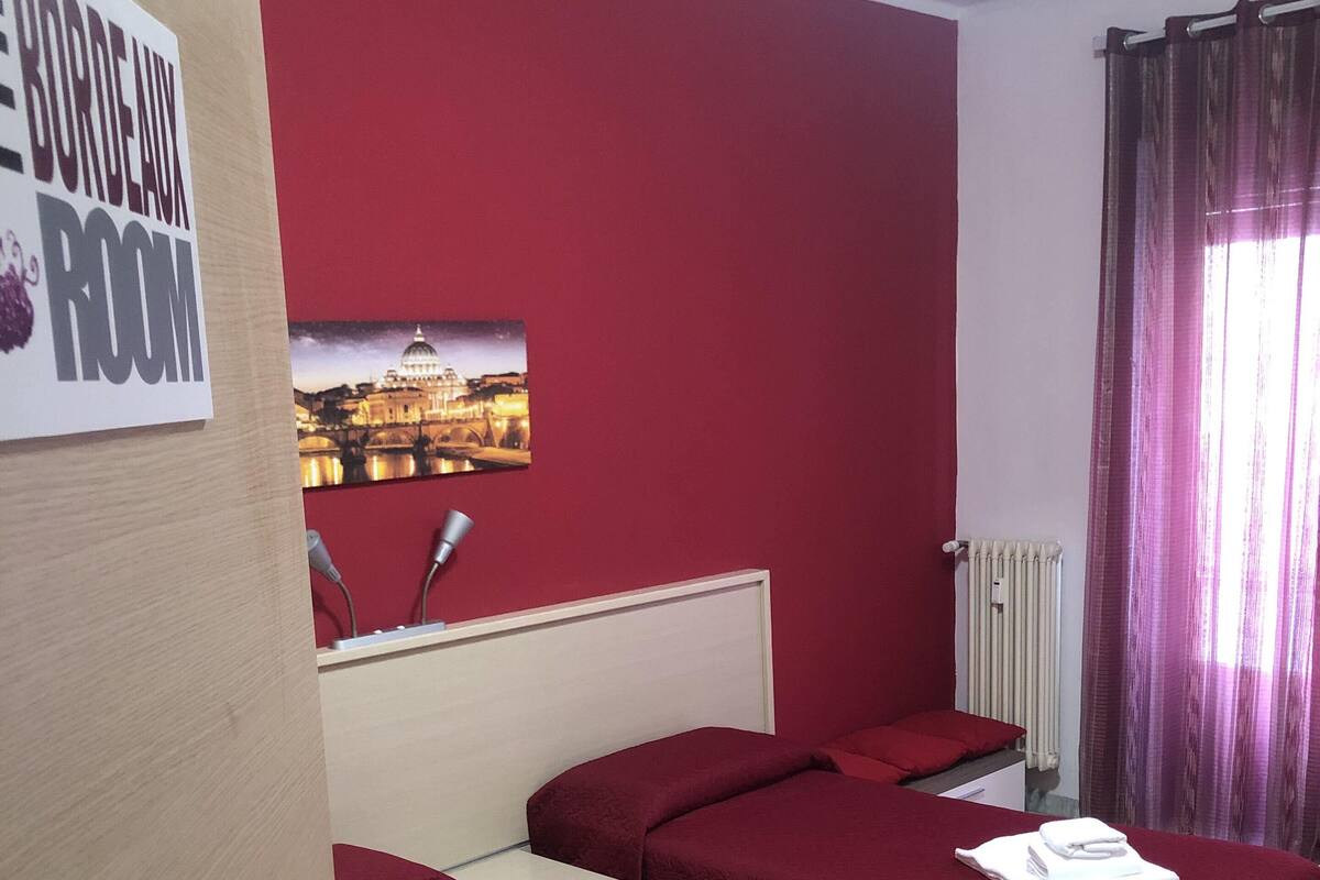 A hotel room with three single beds, a red wall, a picture of a cityscape, and a sign indicating the room type.