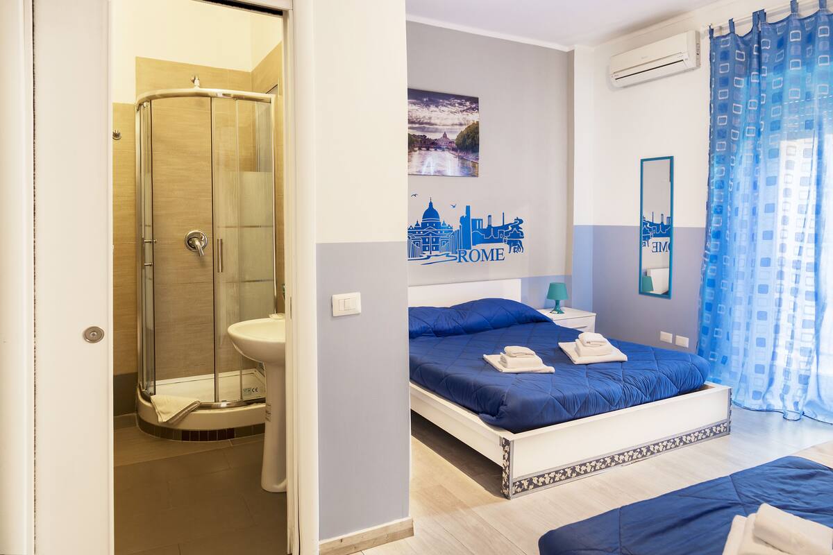A bedroom with a bed, a nightstand, a mirror, and a shower area.