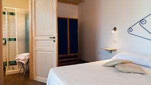 A bedroom with a bed, a nightstand, a wall-mounted shelf, a door, and a bathroom with a bathtub and towel rack. - The Old Farm Asfodeli - Adults Only (Loiri Porto San Paolo)