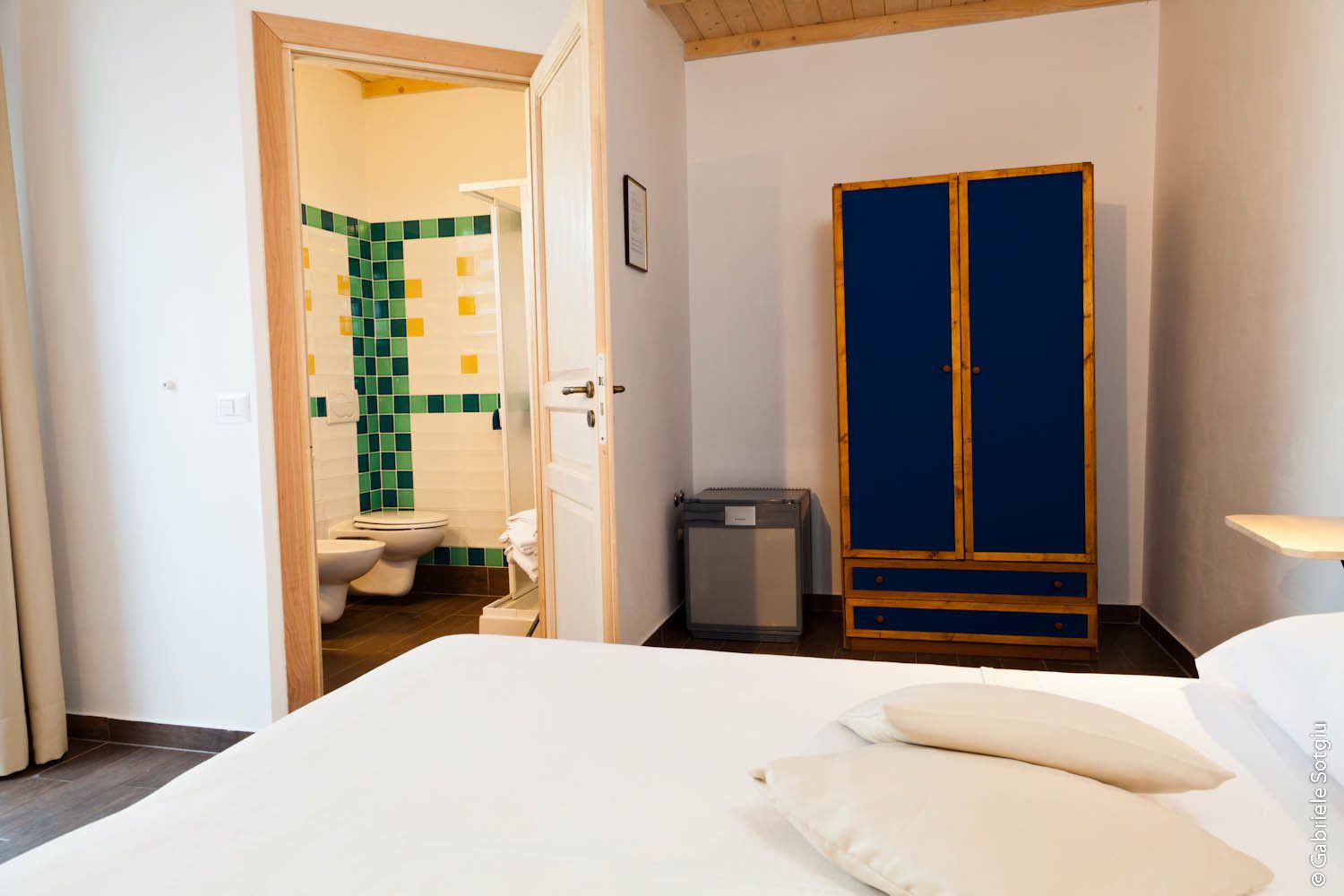 Una camera da letto con un letto, un armadio e un bagno visibile attraverso una porta aperta.