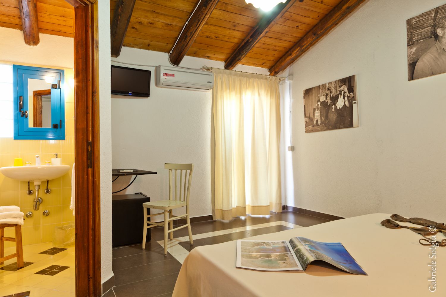Une pièce comprenant un lit, une chaise, une table avec un magazine, un lavabo et un miroir.