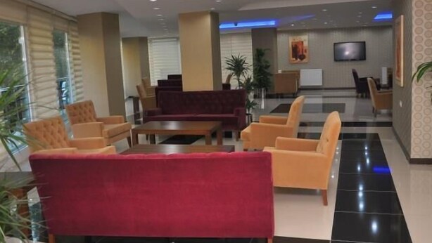 Un vestíbulo de hotel con un sofá rojo, sillones amarillos y una mesa de recepción.