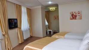 Habitación de hotel con piso de madera, cama con ropa de cama blanca y beige, un cuadro en la pared y una ventana con cortinas.