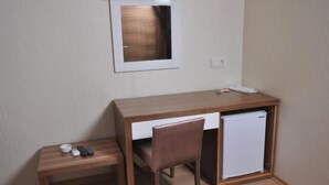 Una habitación compacta con un escritorio de madera, una silla, un refrigerador pequeño y un banco.