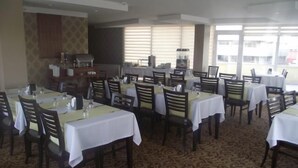 Un comedor con varias mesas y sillas, piso alfombrado y ventanas amplias.