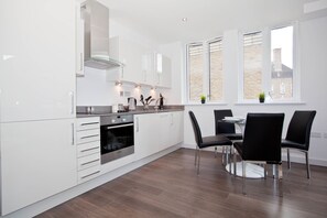 A modern kitchen with white cabinetry, stainless steel appliances, and a dining area with black chairs and a table.