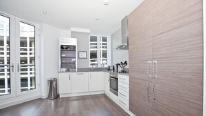A modern kitchen with white cabinets, a stainless steel sink, and a wooden accent wall. - One Whites Row (London)