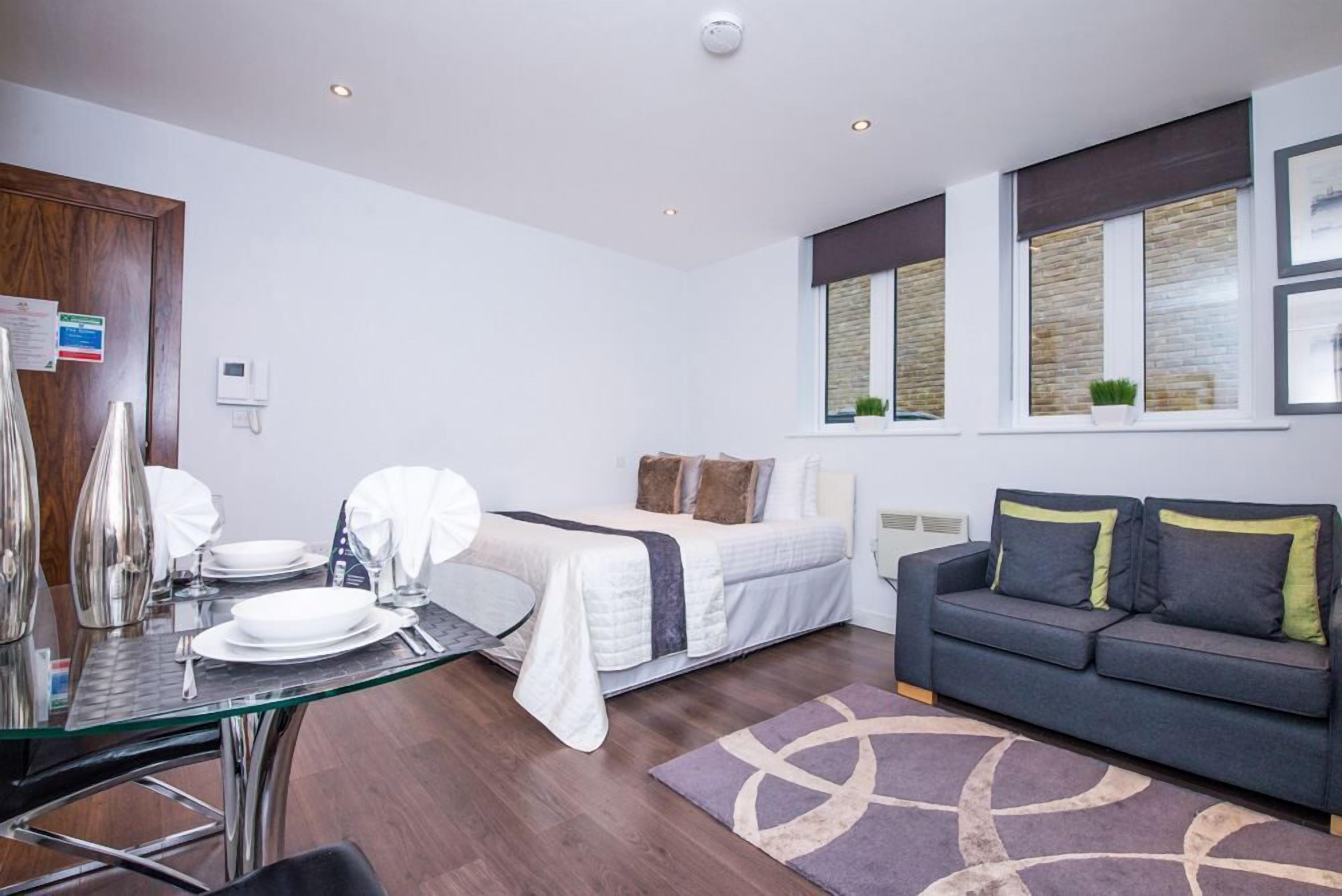 A modern bedroom with a bed, a sofa, and a dining area with a glass table and chairs.