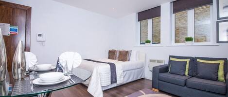 A modern bedroom with a bed, a sofa, and a dining area with a glass table and chairs.