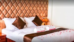 Habitación de hotel con cabecera acolchada, ropa de cama blanca, almohadas marrones y una colcha decorativa rojo y blanco.